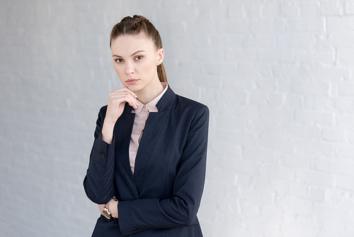 pensive businesswoman in formal wear posing near white wall