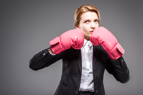 attractive businesswoman in suit and pink boxing gloves, isolated on grey