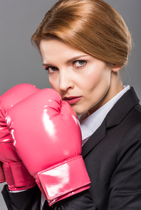 serious businesswoman in suit and pink boxing gloves, isolated on grey