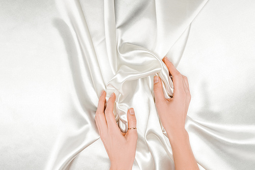 cropped view of female hands gently holding white satin cloth