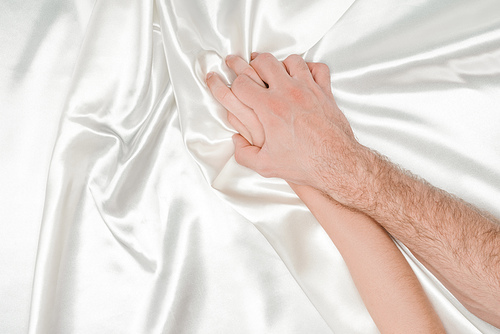 top view of male hand tightly holding female hand on silk white cloth