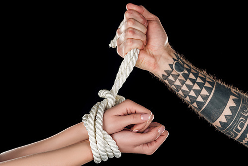 partial view of man tying rope on female hands isolated on black