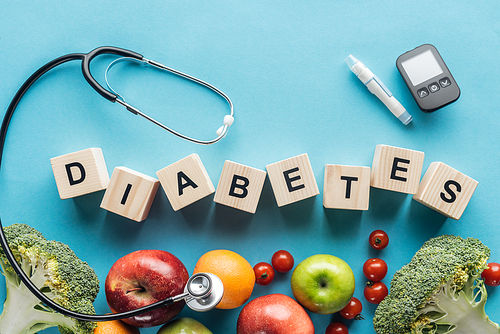 diabetes lettering made of wooden cubes with medical equipment and fruits on blue background