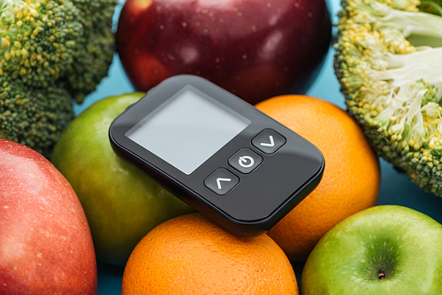 close up view of glucometer among fruits and broccoli on blue background