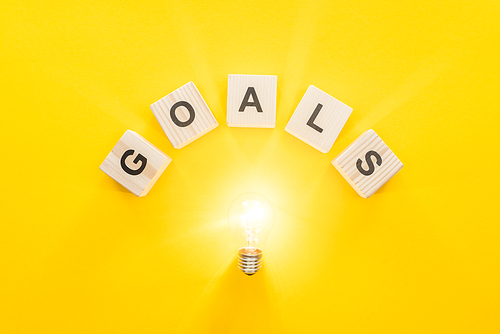 top view of glowing light bulb under 'goals' word made of wooden blocks on yellow background, goal setting concept