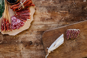 top view of cutting boards with sliced prosciutto, salami and smoked sausages on wooden table  with scattered spices