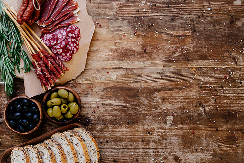 top view of cutting boards with delicious prosciutto, salami, bread, olives and herbs on wooden table  with scattered spices