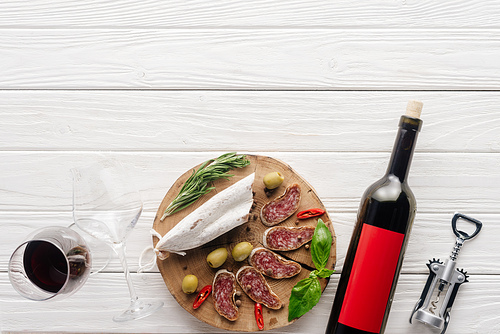 top view of bottle and glass of red wine with assorted meat appetizers on white wooden surface