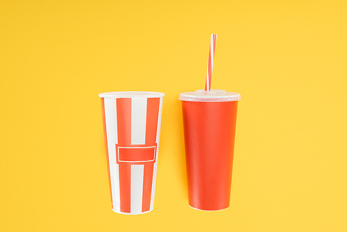 striped popcorn bucket and red disposable cup with straw isolated on yellow