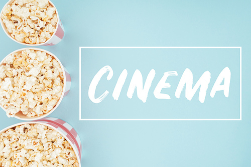 top view of buckets with popcorn in vertical row and cinema lettering isolated on blue