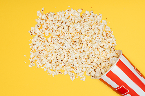 top view of overturned striped bucket with popcorn isolated on yellow