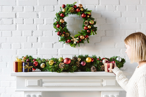 christmas wreath and decorations over fireplace mantel with white brick wall