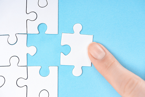 cropped shot of woman pointing at white puzzles pieces on blue background