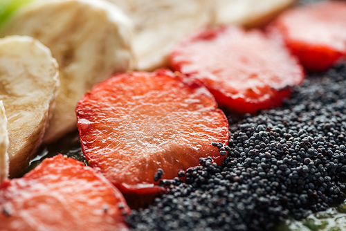 selective focus of sliced organic bananas, strawberries and poppy seeds