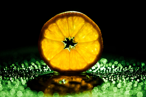slice of orange on black background with green bokeh and backlit
