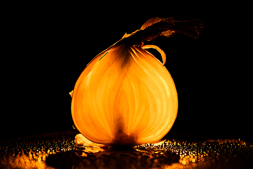 slice of raw onion with water drops and orange back light on black background