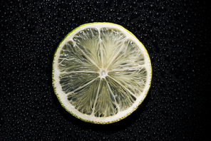 slice of fresh lime on black background with water drops