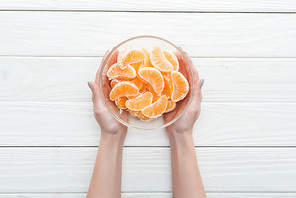 cropped view of woman holding glass bowl with tangerine slices on wooden white background