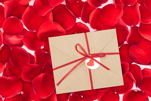 top view of envelope with ribbon and red rose petals on background, st valentines day concept