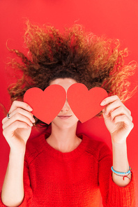 top view of girl holding heart shaped cards in front of face isolated on red, st valentines day concept