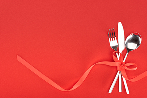 view from above of fork, knife and spoon wrapped by red festive ribbon isolated on red, st valentine day concept