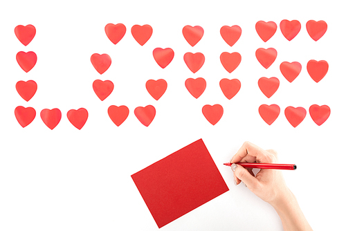 cropped image of woman writing greeting card under lettering love made of red heart symbols isolated on white, st valentine day concept