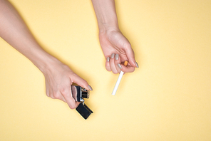 Partial view of woman holding cigarette and cigarette lighter isolated on yellow
