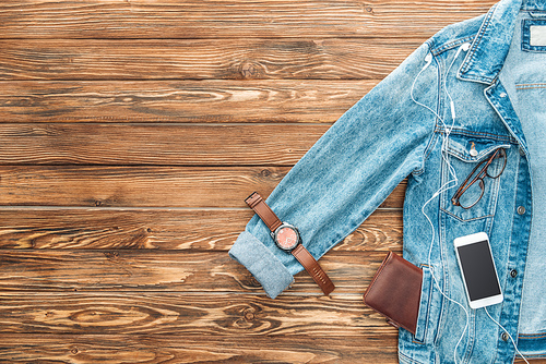 Top view of denim jacket, wristwatch and smartphone on wooden background