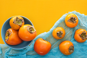 top view of whole orange persimmons on blue plate and cloth