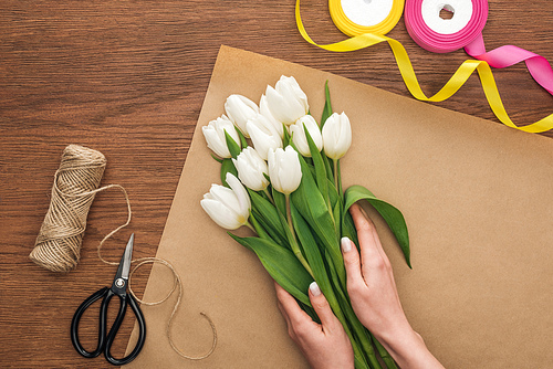 cropped view of on florist making bouquet of white tulips on wooden background