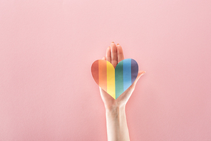 cropped view of woman holding rainbow colored paper heart on pink background, lgbt concept