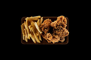 top view of tasty french fries and chicken nuggets on plate isolated on black