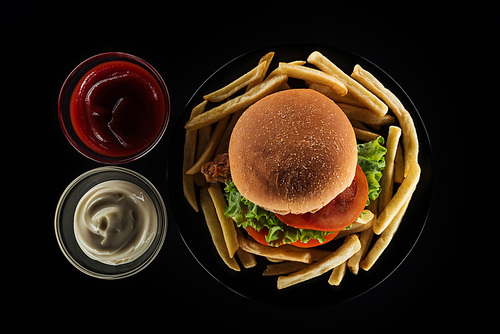 top view of tasty french fries and chicken burger near mayonnaise and ketchup isolated on black