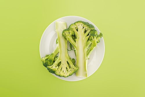 top view of tasty organic broccoli on white plate isolated on green