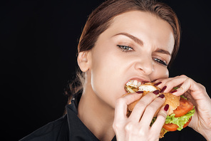 angry woman eating tasty chicken burger isolated on black
