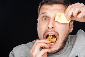 man covering eye with chip while eating isolated on black