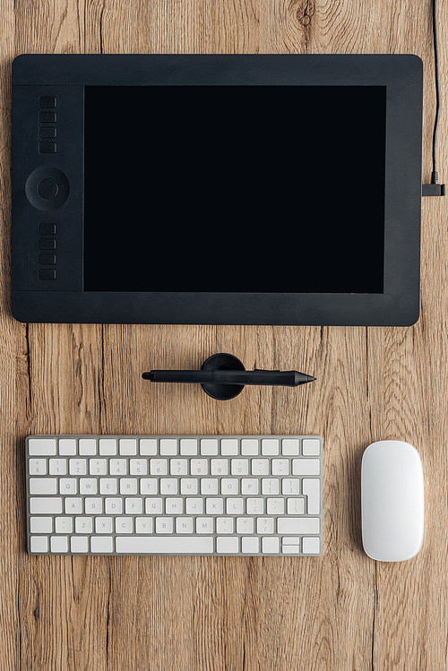 top view of graphic tablet, graphic pen, wireless computer keyboard and computer mouse on wooden table