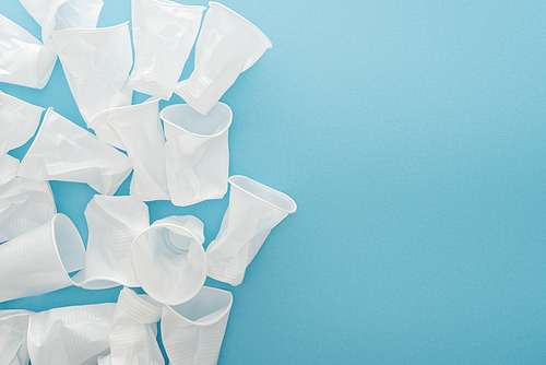 top view of white and crumpled plastic cups on blue background with copy space