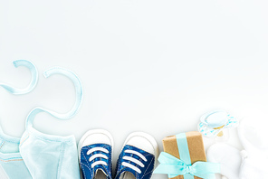 top view of booties and sneakers, pacifier, gift box and bonnet on white background