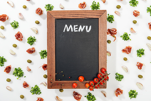 chalk board with menu lettering among prosciutto, olives, garlic cloves, greenery and cherry tomatoes