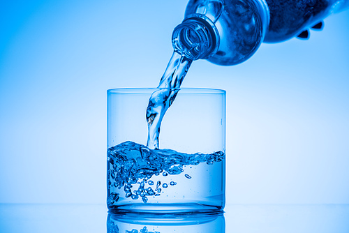 cropped view of man pouring water from plastic bottle in glass on blue background
