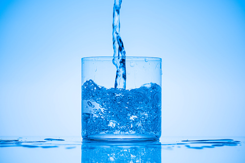 toned image of water pouring in  glass on blue background with splashes