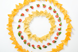 top view of sliced chili peppers and tasty nachos with basil leaves on white background