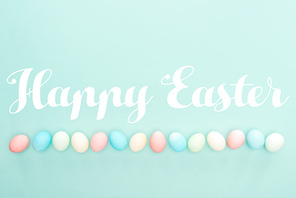top view of pastel painted eggs in row with Happy easter lettering isolated on blue