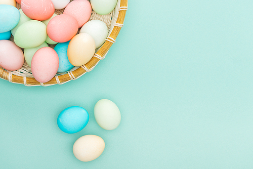 top view of traditional pastel easter eggs in wicker plate isolated on blue with copy space