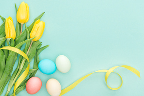 top view of yellow tulip flowers with ribbon and easter eggs isolated on blue with copy space