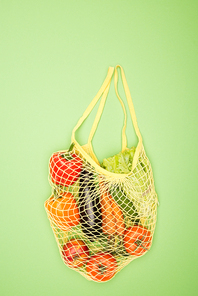 top view of yellow string bag with ripe organic vegetables on light green surface with copy space