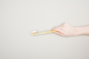 cropped view of woman holding bamboo toothbrush with toothpaste on grey background