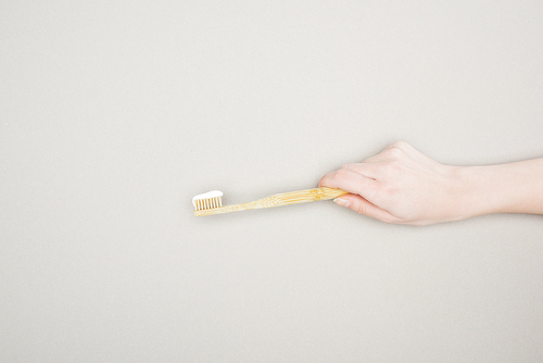 cropped view of woman holding bamboo toothbrush with toothpaste on grey background