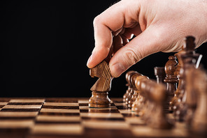 cropped view of man doing move with knight on wooden chessboard isolated on black